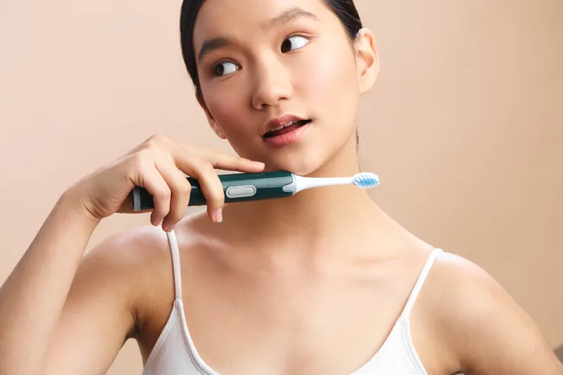 Asian woman smiles softly as she brushes her teeth, capturing a clean morning routine in a bright bathroom. The scene emphasizes wellness, personal care, and a calm, healthy lifestyle with a focus on