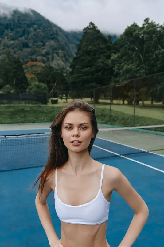 Young athletic model in a white sports bra on a tennis court, showcasing fitness and confidence against a vibrant outdoor background