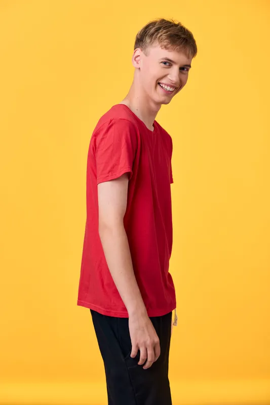 Smiling youth in a red shirt, casual fashion pose against a bright yellow background, radiating confidence and energy, ideal for lifestyle and fashion themes in stock photography.