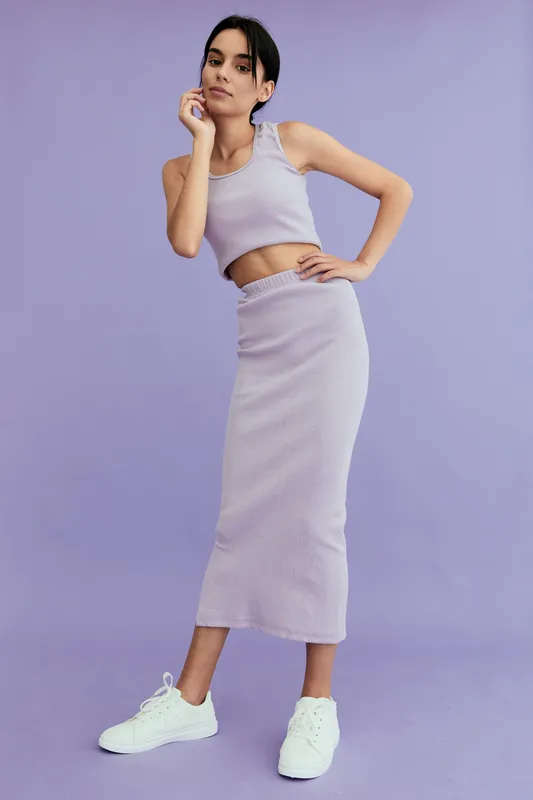 young woman in casual purple outfit posing confidently against lavender background, wearing white sneakers and relaxed expression