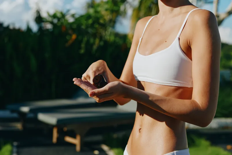 Active woman outdoors, wearing a white sports bra, holding a small object in her hands, sunlit moment, warm breeze, natural colors, relaxed lifestyle and fitness vibe, candid