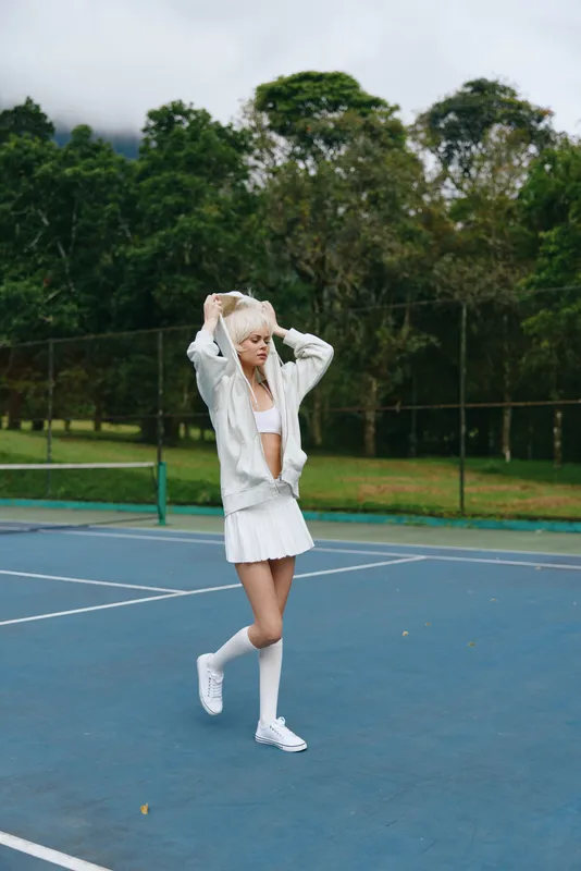 Young female athlete in sporty outfit, enjoying a moment on the tennis court, showcasing confidence and determination in a vibrant outdoor setting