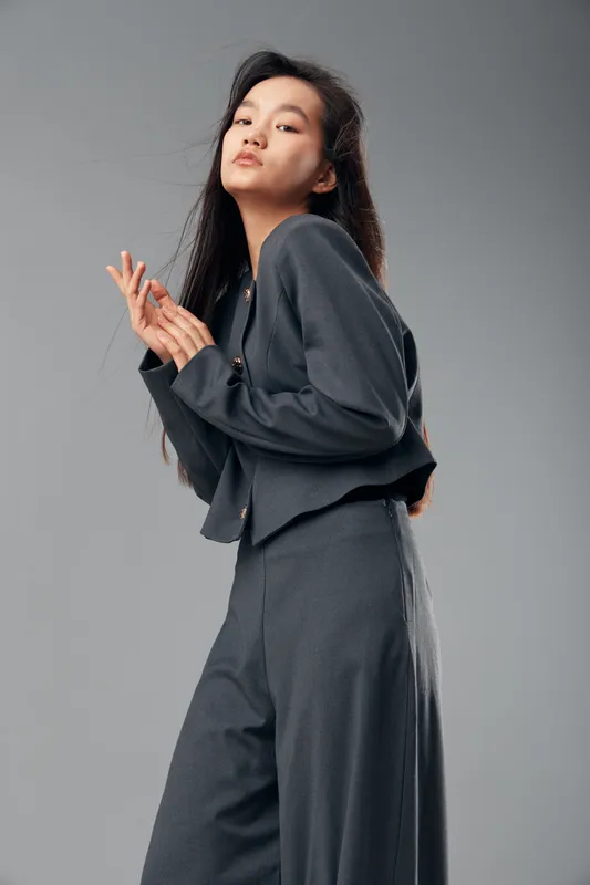 Young woman in gray suit posing with confident expression in studio space. Fashion model with long dark hair wearing stylish outfit for portrait photography concept.