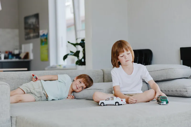 Two playful boys engage in imaginative play with toy cars in a cozy living room, showcasing a blend of creativity and fun in a homely environment.