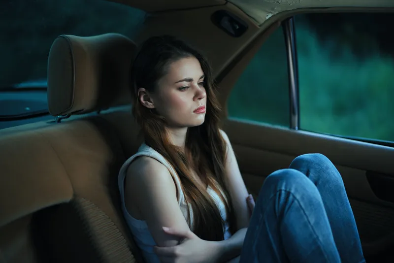 A young woman with long hair sitting in a car, looking out the window with a pensive expression, embodies a feeling of introspection and solitude.