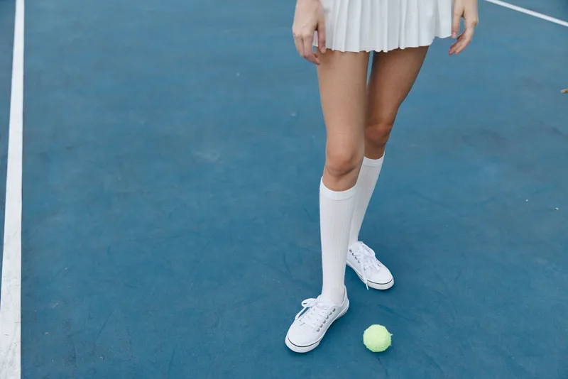 Young female athlete in white tennis outfit on blue court, showcasing energy and focus Tennis ball nearby highlights the sport and action