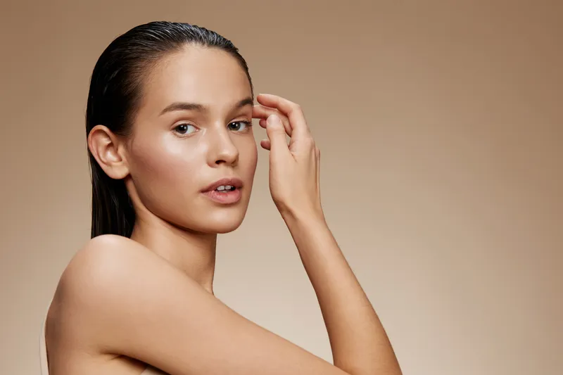 Young woman with smooth skin and wet hair, showcasing natural beauty, against a neutral beige background, embodying health and self care
