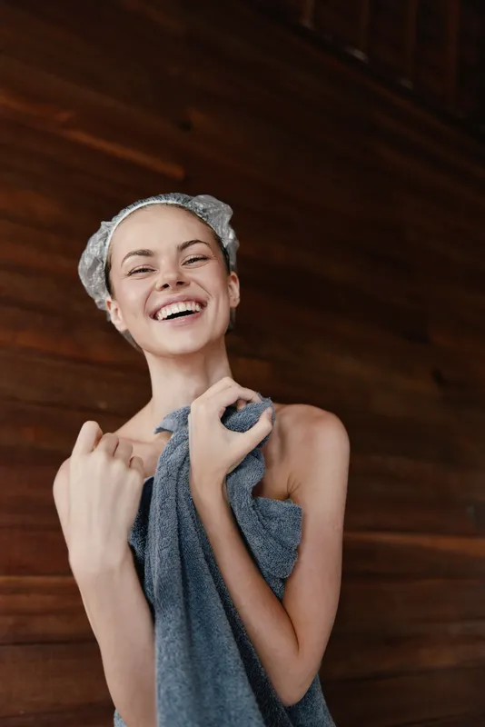 smiling woman holding towel happy and relaxed after sauna session with wooden background wellness and self-care concept
