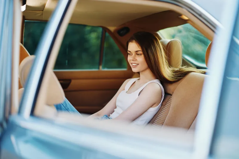 Young woman relaxing in the car during a sunny day, showcasing a carefree expression and casual style in a warm, natural setting.