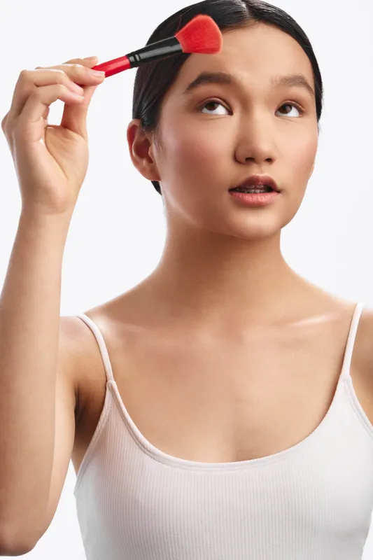 asian woman applies makeup with a brush in a clean studio setting, a focused expression and soft lighting create a calm, professional scene that highlights beauty preparation, self care, and mindful