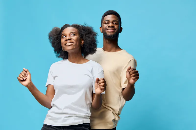 Joyful young couple dancing together against a bright blue background, showing happiness and connection in a casual setting