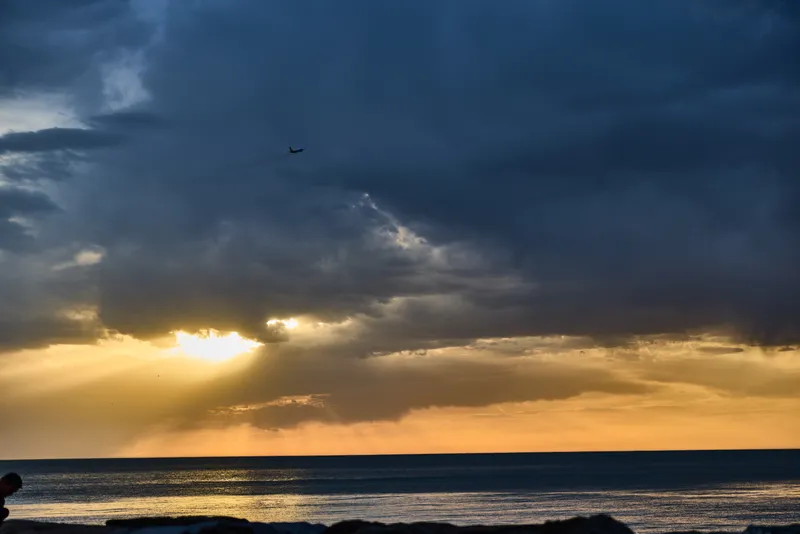 Confident woman in business attire looking at the ocean, exuding determination under a dramatic sunset, capturing the essence of ambition and tranquility.