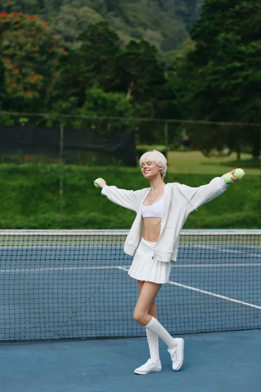 Joyful female tennis player with a short white outfit celebrating victory on a sunny court, showcasing fitness and energy