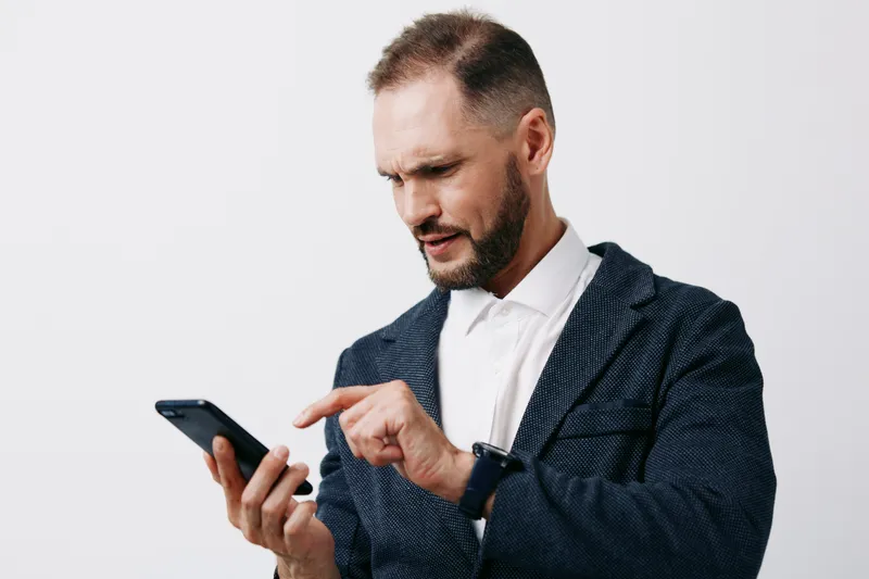 A focused businessman checks his phone, projecting confidence and concentration. He stands against an isolated colored background, creating a professional mood and clear, calm emotion.
