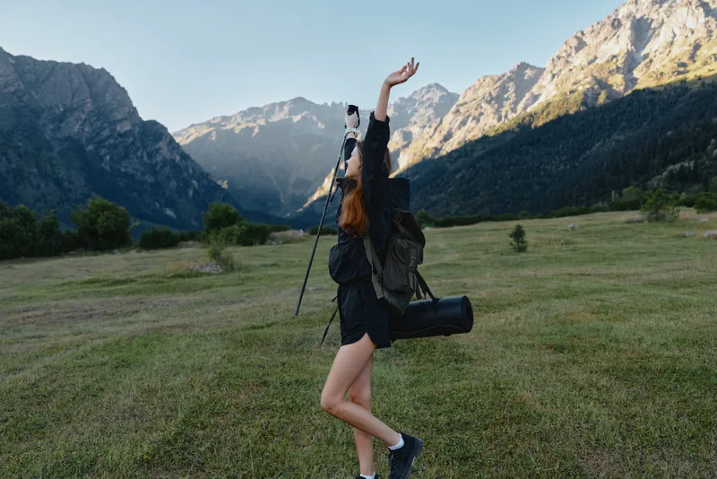 A young photographer in a field raises a camera toward the mountains, capturing the moment with enthusiasm and energy in a wide open landscape, conveying adventure and vigor.