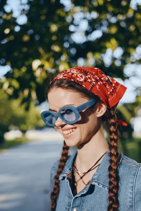 Lifestyle woman wearing modern boho-western denim street style with braided hair and a red bandana, smiling outdoors in warm natural light with film color tones.