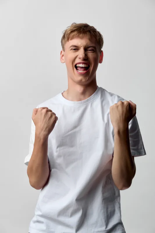 Excited young man in a white t shirt celebrates with clenched fists raised, conveying confidence, energy, and a moment of triumph and motivation