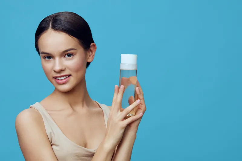 Young woman with glowing skin holding a skincare product against a blue background, showcasing beauty, wellness, and healthy lifestyle