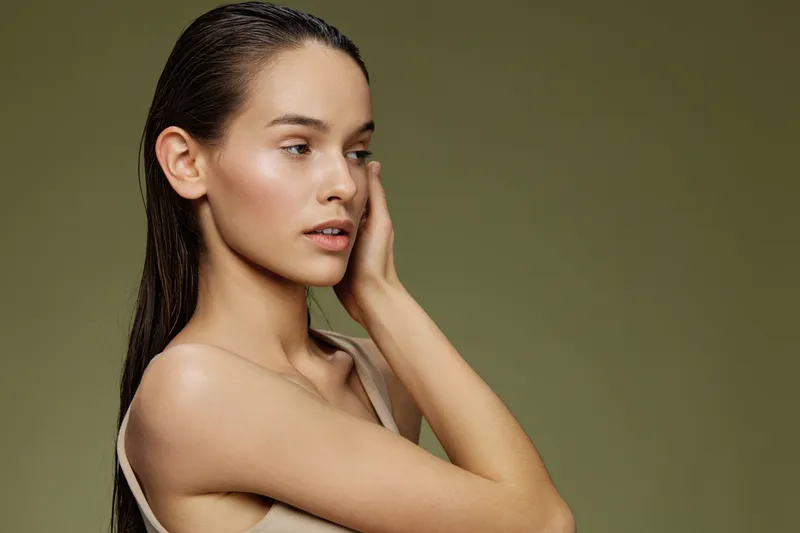 Elegant young woman with wet hair poses thoughtfully against a muted green background, evoking beauty and tranquility in fashion photography