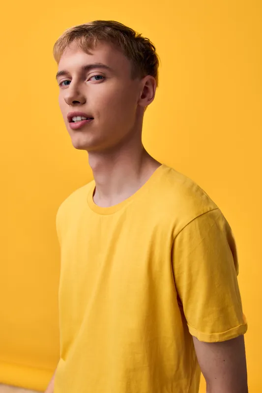 Yellow shirted male model in a bright studio with a vivid yellow backdrop, casual fashion pose, soft lighting and confident expression, modern lifestyle imagery for branding.