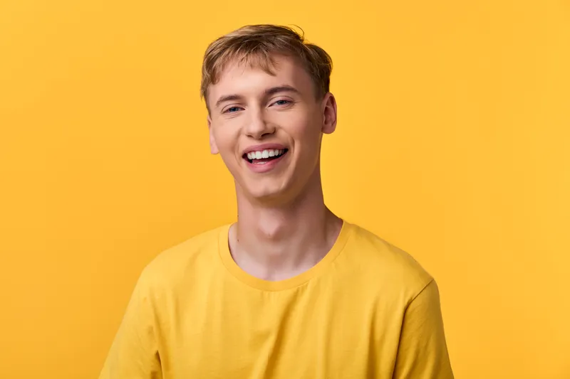 Smiling man in a yellow shirt against a bright yellow background, conveying friendliness, joy, and positivity for lifestyle, fashion, or marketing visuals