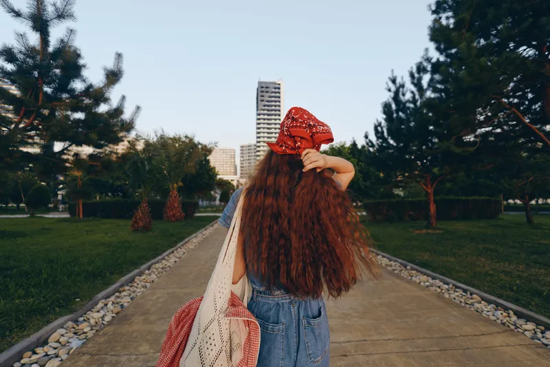 lifestyle woman in modern boho-western denim street style walking outdoors with long hair and red bandana in warm film color tones