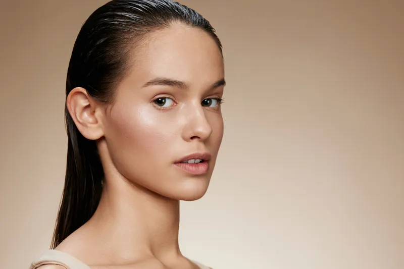 Young woman with wet hair and natural makeup on a neutral background, expressing confidence and serenity, perfect for beauty and skincare concepts