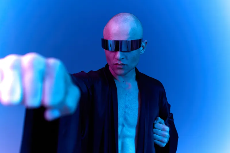 A confident man in a futuristic outfit striking a powerful pose under blue lighting, showcasing a strong, dynamic presence in a modern setting.