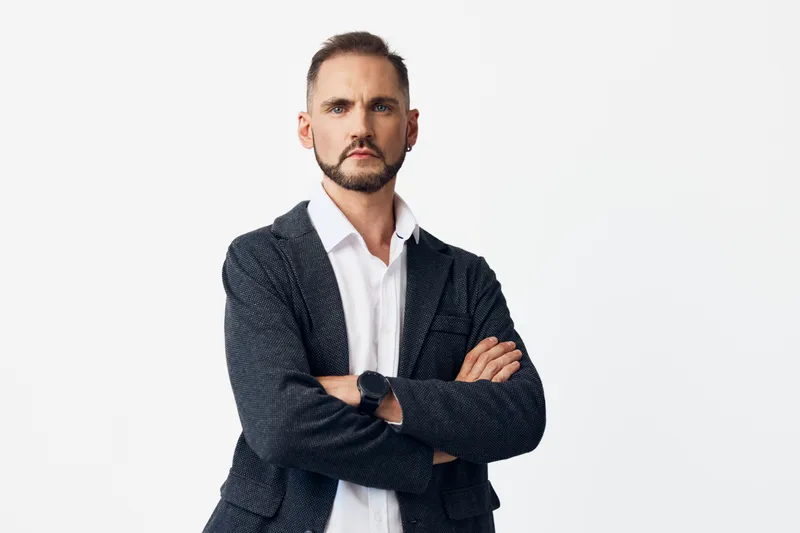 A confident business professional man poses with arms crossed against a clean white background, projecting focus, strength, authority, and steady determination.