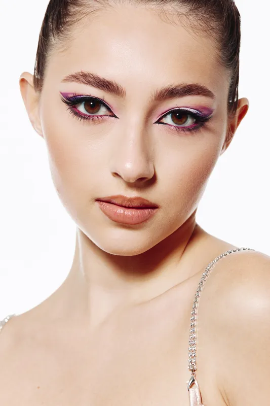 Close-up portrait of a young woman with creative pink eyeliner makeup and flawless skin wearing a sparkling outfit. Bright beauty shot with fashionable and artistic flair.