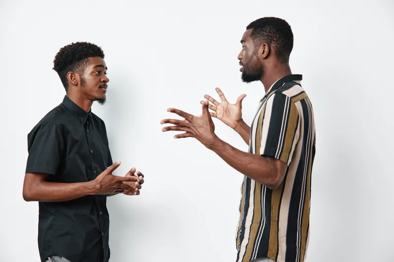 Two african american men with dark skin having serious conversation and discussion in casual clothes on white background in studio setting.