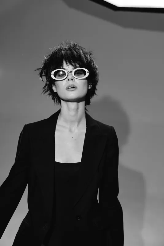 Black and white portrait of a stylish woman wearing sunglasses and a black blazer with a confident expression.