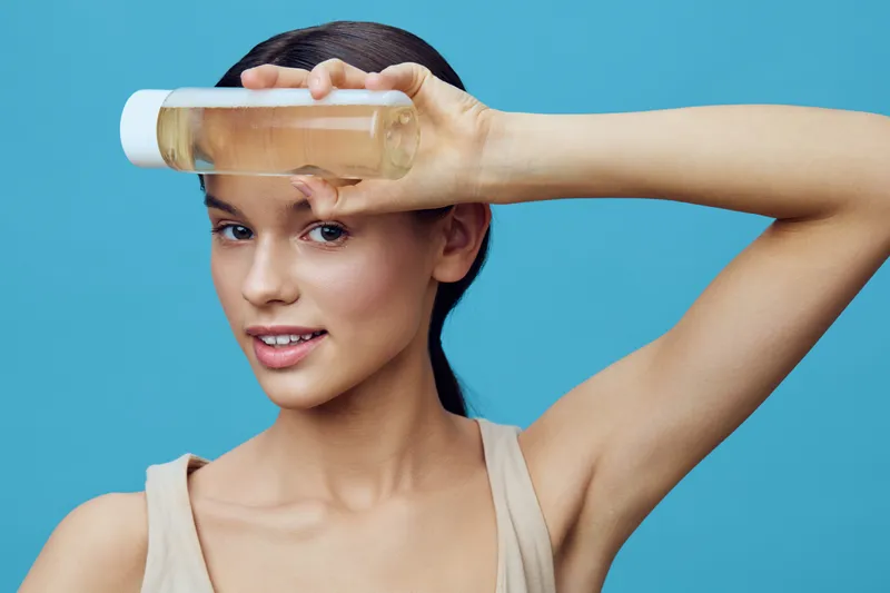 Young woman showcasing a skincare product, expressing happiness, against a blue background, promoting beauty and self care in wellness lifestyle