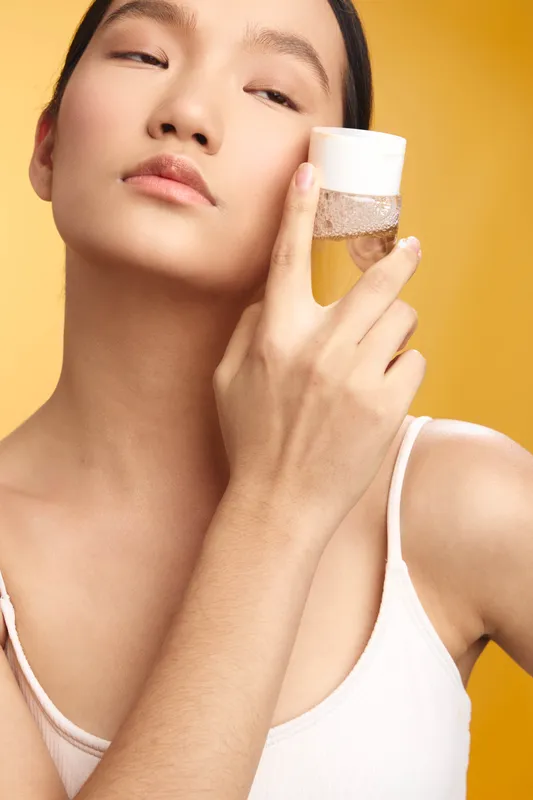 asian woman applies skincare product in a bright studio, showcasing calm confidence, healthy complexion, and modern self care aesthetic. Soft lighting highlights smooth skin and a tranquil routine.