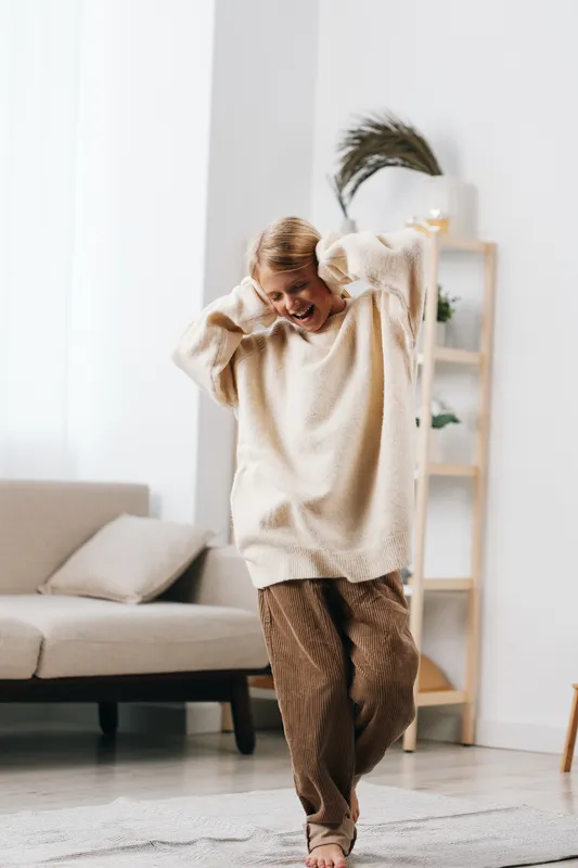 Authentic lifestyle scene featuring a young person at home, joyful play theme, casual school inspired attire, soft natural light, cozy textures, candid movement, and relaxed atmosphere.