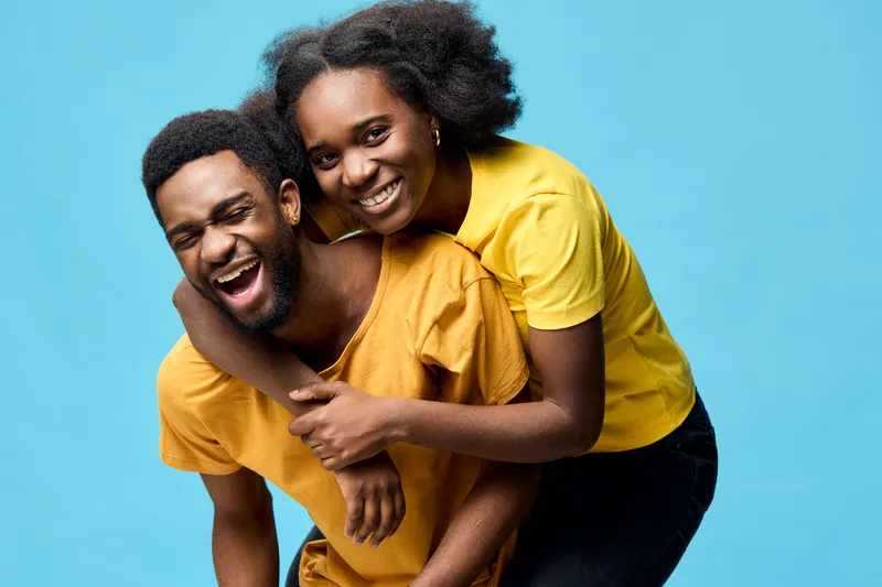Happy couple in yellow and blue, laughing and embracing, celebrating love and connection, with a vibrant blue background enhancing their joy and energy