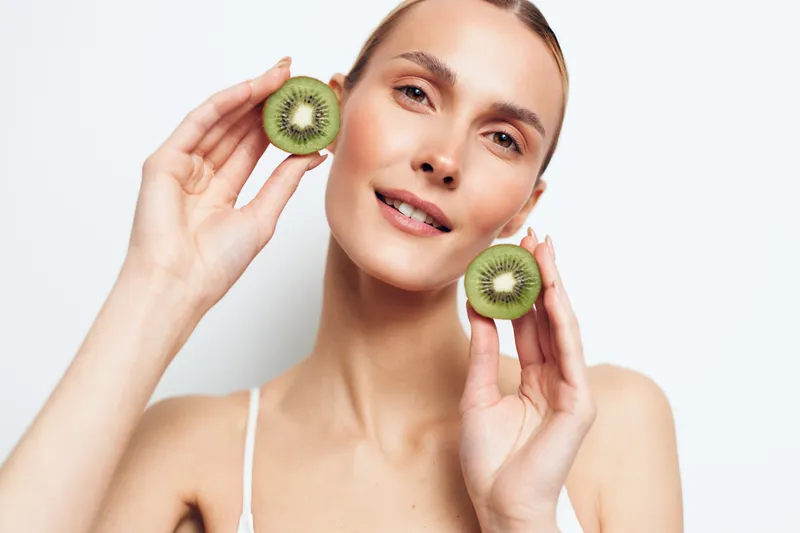 Woman holding kiwi pieces, fresh beauty skincare concept for healthy fruit portrait, natural glow, smiling with calm expression, clean studio light, minimal background, soft shadows, copy space