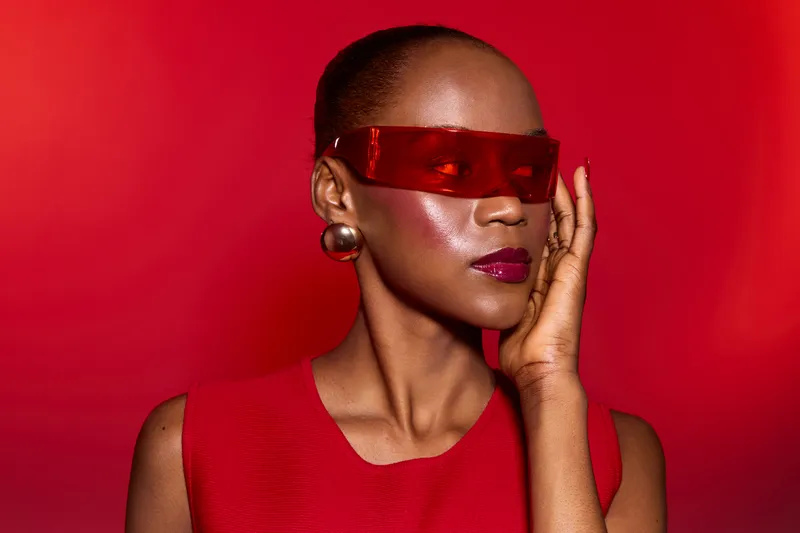 Stylish African American woman with dark skin wears red sleeveless top and red futuristic sunglasses on bright red background. Concept for fashion, beauty, and modern style.