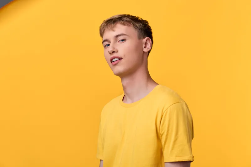 Young man in a yellow t shirt poses against a solid yellow background, conveying casual style, confident expression, and bright mood for fashion and lifestyle usage