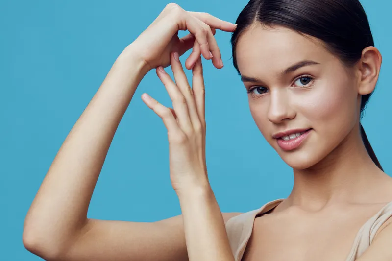 Elegant young woman with a natural smile against a light blue background, showcasing soft skincare and beauty trends, emphasizing confidence and grace