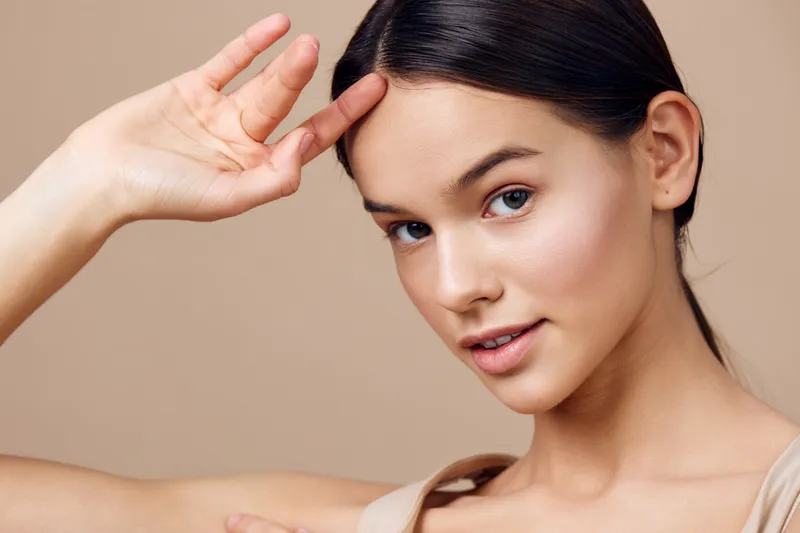 Portrait of a young woman with a natural makeup look, demonstrating beauty and confidence against a soft beige background, perfect for beauty and skincare concepts