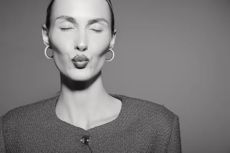 Young white woman with fair skin and earrings makes a kiss face with closed eyes in studio.