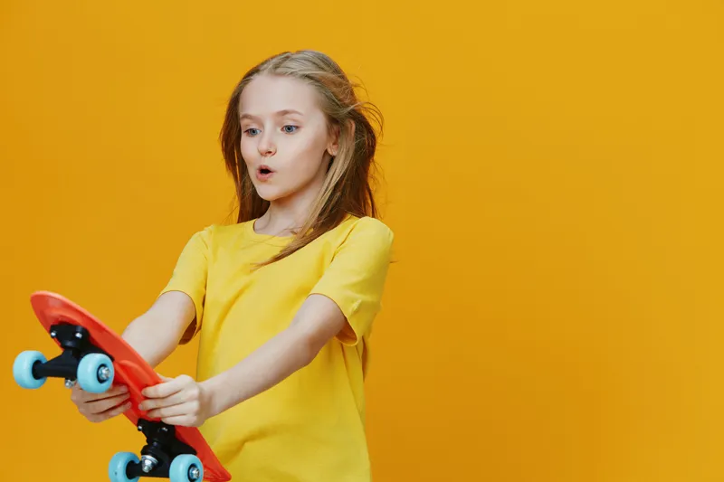 A girl in a yellow shirt surprised by her skateboard against a bright yellow background, capturing joy and excitement in a playful atmosphere