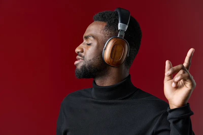 Young African man enjoying music with headphones against a vibrant red background, expressing joy and relaxation in a stylish black turtleneck sweater