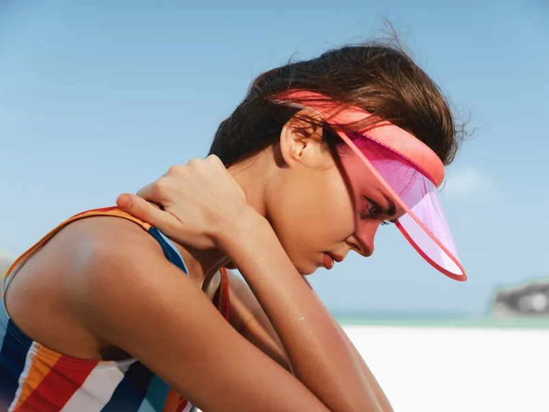 Athlete on a sunny beach wearing a pink visor, close up profile, sunlit skin and toned shoulders, vibrant sporty outfit, calm posture, focused expression.