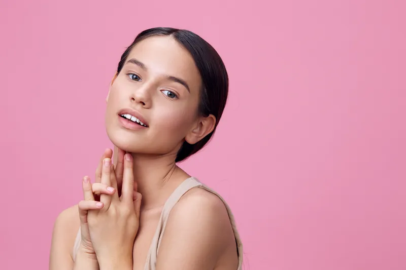 Young woman with clear skin and natural makeup against a soft pink background, evoking freshness and beauty in fashion and portrait photography