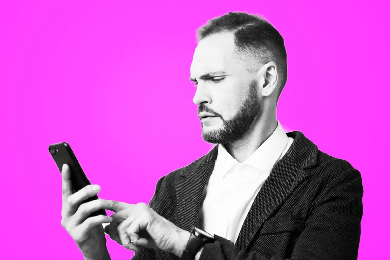 A professional businessman stands against a vibrant pink background, focused on his smartphone, conveying confidence, concentration, and a modern work mindset.
