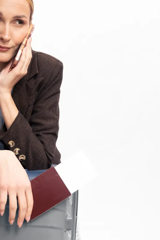 Young woman in brown jacket holding passport and plane ticket while talking on phone. Concept of travel planning, vacation preparation, and communication. White background with copy space.