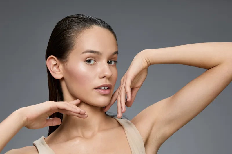 Young woman with a fresh look and natural beauty poses elegantly, showcasing flawless skin and a captivating expression against a neutral background