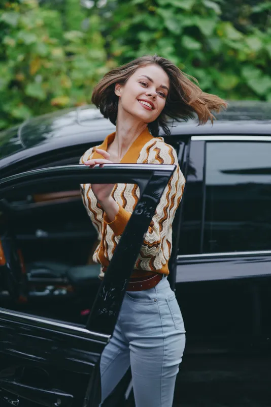 A cheerful woman steps from a sleek car, smiling with confidence as she opens the door, ready for a sunny day adventure and new experiences on the road.